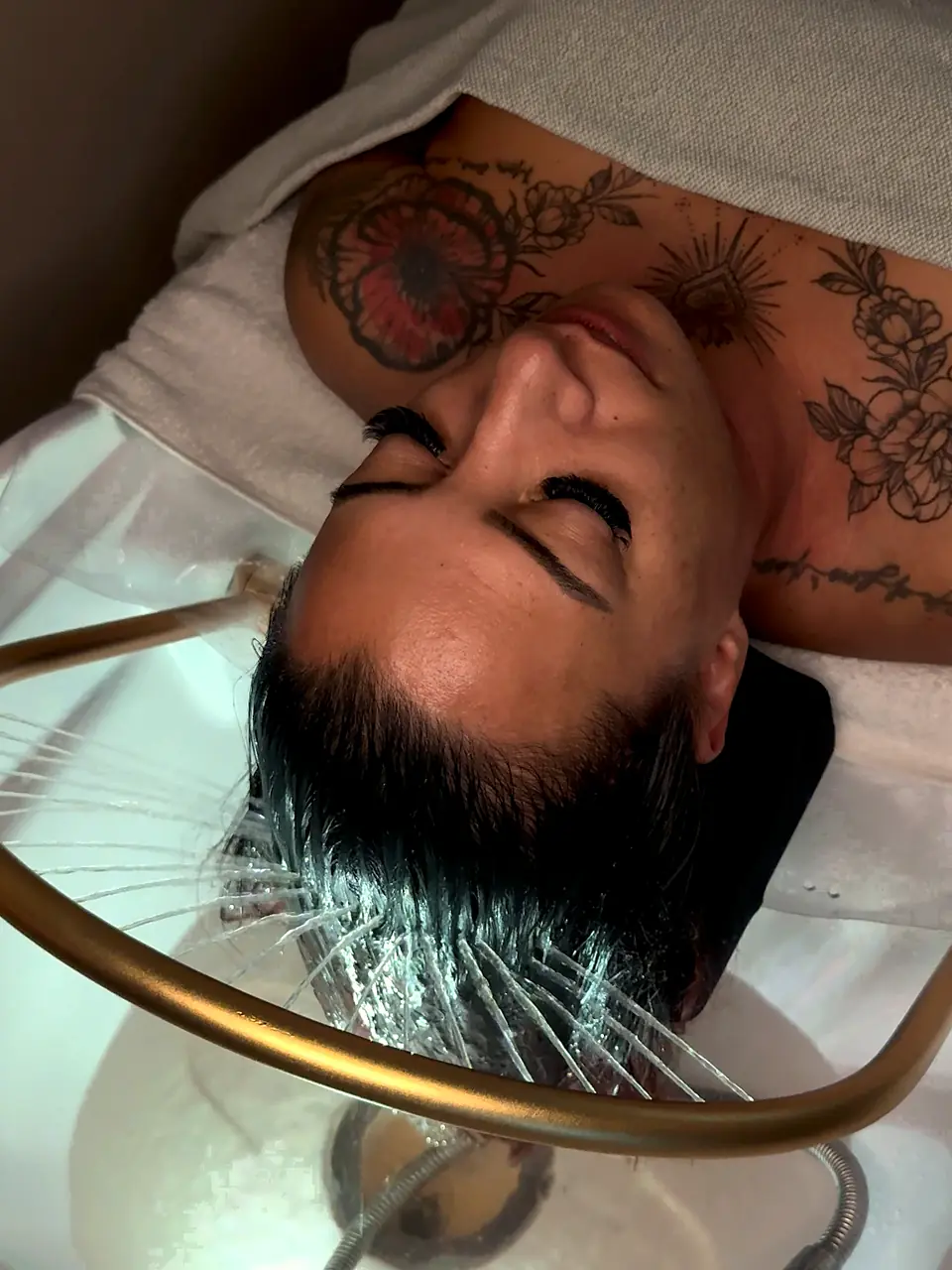 Cliente détendue sous l’arceau doré du bac, avant le modelage et le rituel head spa