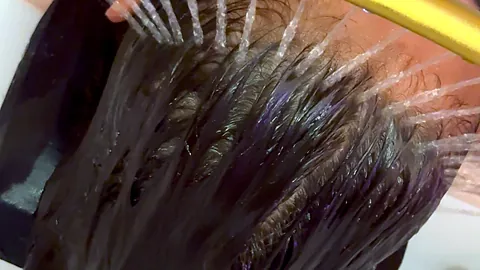 Cheveux longs rincés dans le bac sous l’arceau doré, lumière naturelle